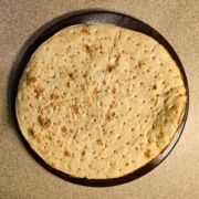 Pre-cooked pizza crust on a freshly oiled pizza stone