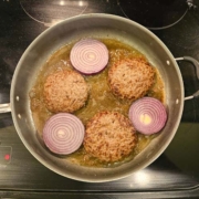 burgers and onions frying in a skillet